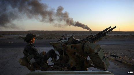 Libyan rebel fighter with burning oil refinery in the distance, Ras Lanuf, August 2011