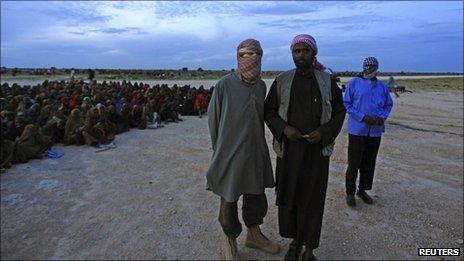 Al Shabaab"s spokesman Sheikh Ali Mohamud Rage (R) and a foreign al-Qaeda official Abu Abdalla al Muhaajir (L) watch as food rations from al-Qaeda are distributed at the Ala-yasir Internally Displaced People (IDP) camp for al-Shabab militias, in Lower Shabelle, 50 km (31 miles) south of Somalia"s capital Mogadishu, October 13, 2011.