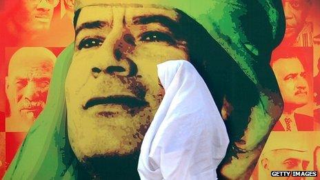 A woman walks past a image of Colonel Gaddafi