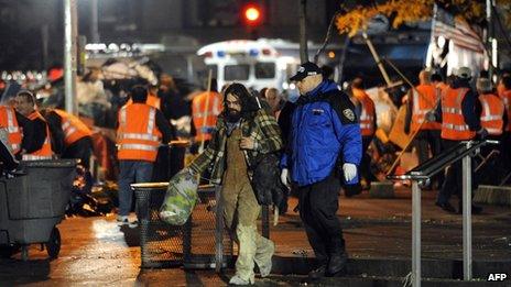 A man is escorted by a New York Police Department officer as New York City sanitation workers clear Zuccotti Park