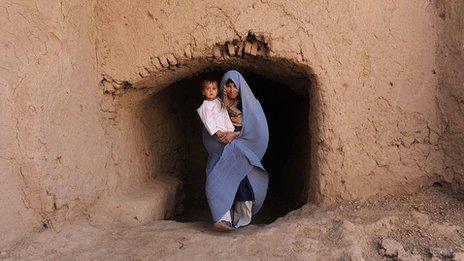 Afghan woman holds her baby as she walks in the outskirts of Herat in October 2011