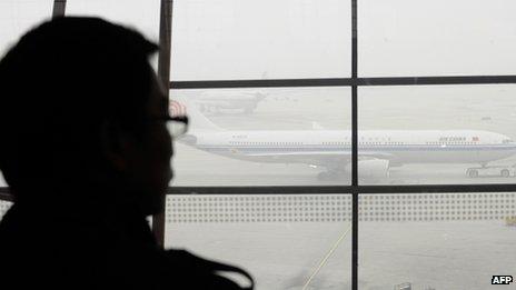 A traveller looks out at an airplane shrouded in smog at Beijing International Airport