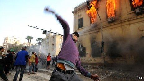 An Egyptian protester hurls a stone at security forces as a building burns in Cairo, 18 December