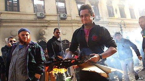 A man removes burning books from the destroyed Institute of Egypt