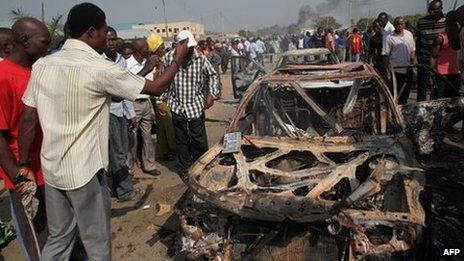 People gather around burnt cars near St Theresa Catholic Church after a bomb blast in the Madala Zuba district of Nigeria's capital Abuja on 25 December 2011. Two explosions near churches during Christmas Day services in Nigeria, including one outside the country's capital, killed at least 28 people amid spiralling violence blamed on an Islamist group.