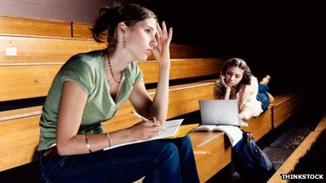 Students in lecture hall, one with exercise book, the other with a laptop