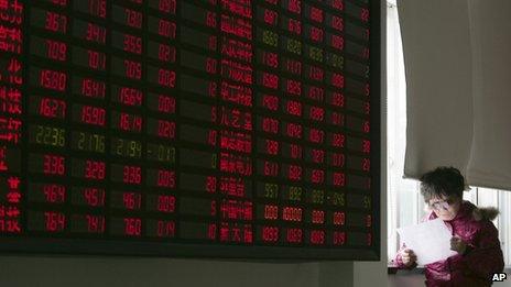 An investor looks at a document next to the stock price monitor at a private securities company Friday Jan. 20, 2012 in Shanghai, China