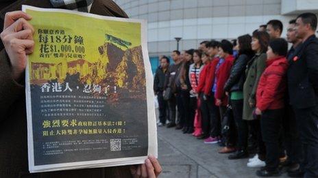 An unidentified woman holds the newspaper advertisement, as a group of mainlanders pose for a picture in the background on 1 February 2012