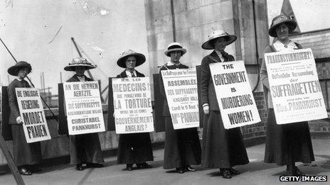 A group of suffragette women demonstrating with placards, in English, French and German, condemn the British government