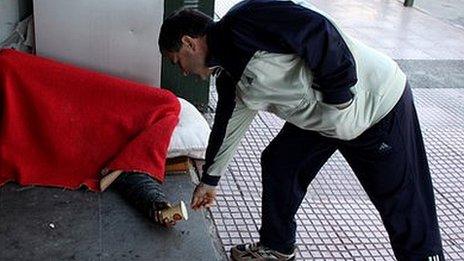 man gives coin to homeless person under a blanket