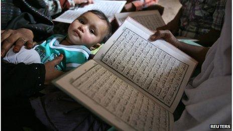 Survivors read the Koran as a child looks on during the commemoration of the 10th anniversary of Godhra riots in the western Indian city of Ahmedabad February 27, 2012