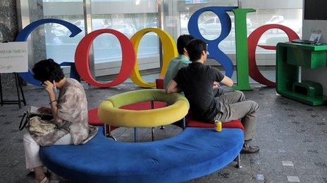 People sit on a sofa in front of a Google logo