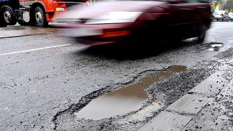 A car drives past a pothole