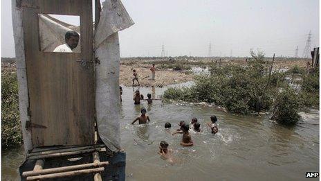 This May 12, 2006 file photograph shows a slum resident (L) as he uses a toilet that opens into the water below as children swim in the water near a protest rally against the government for demolishing make-shift huts at Mandala in Mankhurd in north central Mumbai.