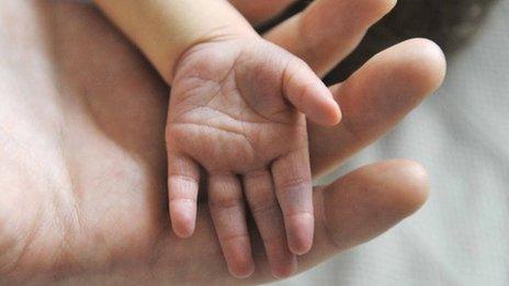 An adult holding a newborn babies hand.