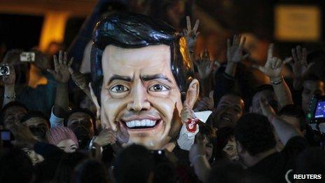 A large figure of Enrique Pena Nieto's head surrounded by crowds at a rally