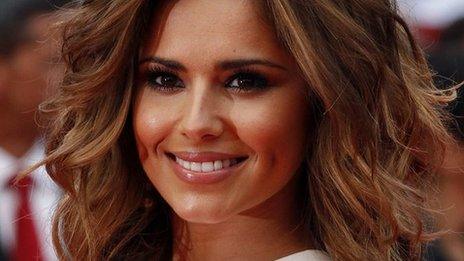 Cheryl Cole appears at a recent film premiere. She has a beaming smile. Her hair is now light brown and lightly curled.