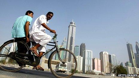 Foreign workers cycle past Dubai skyscrapers