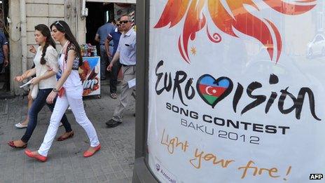 Women walk past a sign for Eurovision 2012