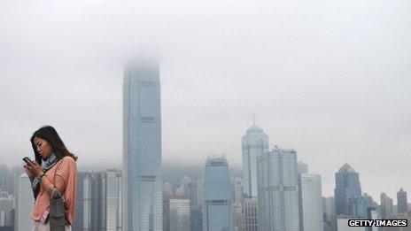 A woman uses her mobile, with Hong Kong skyline in the background