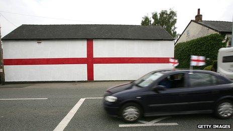 A car with flags drives past a giant flag of St George that has been painted on the side of a house ahead of the 2006 World Cup.