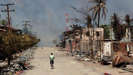 A resident rides her bicycle past burned houses in Sittwe, June 12 2012