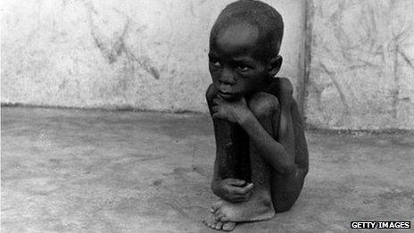 A naked child squats on a pavement