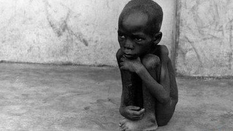 A naked child squats on a pavement