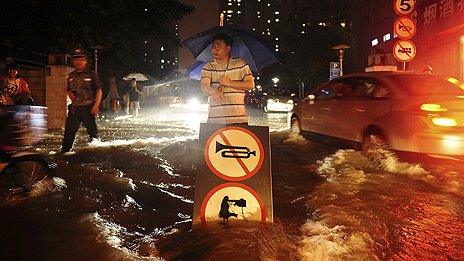 A Chinese man uses a signboard to signal motorists driving through flooded street following a heavy rain in Beijing Saturday, July 21, 2012