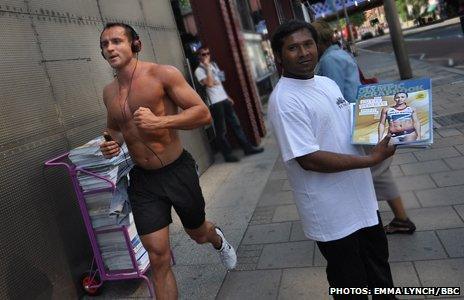 A vendor hands out Olympic scrapbooks as a man runs by