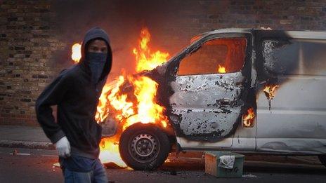 A hooded youth walks past a burning van in Hackney on 8 August 8, 2011