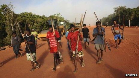 Brazilian indigenous walk past heavy machinery