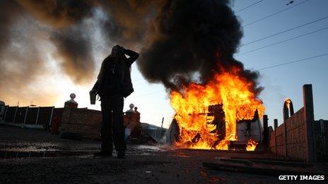 An activist looks on in front of a burning caravan, which was set ablaze by activists to be used as a barricade, as evictions began at Dale Farm travellers camp on 19 October last year