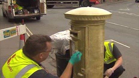 The post box being painted gold in Hay-on-Wye