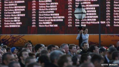 People gather before giant screen displaying names of the 96 victims