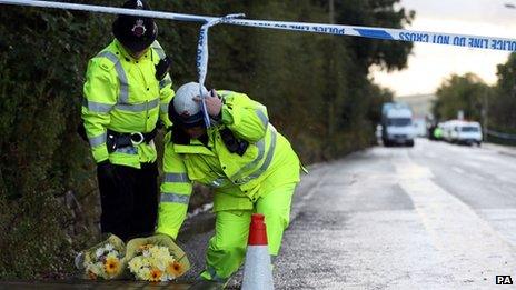 Police officers collect flowers at the scene of the Mottram shootings