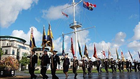 Canadian flag flies on Guernsey memorial mast as parade of standards walk past