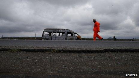 A mineworker walks past the remains of a minibus taxi burnt in strike related violence close to a mine belonging to Anglo American Platinum outside Rustenburg in the North West province, 12 October, 2012