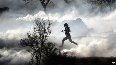 A Palestinian demonstrator runs through a cloud of tear gas during clashes against Israel's operations in Gaza Strip, outside Ofer, an Israeli military prison near the West Bank city of Ramallah