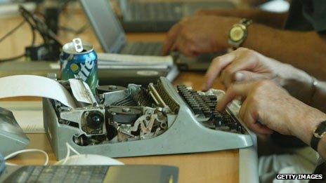 Reporter on a typewriter surrounded by those on laptops