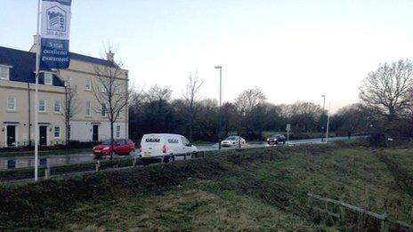 Cars drive on the pavement to avoid floodwater on Lobleys Drive in Brockworth