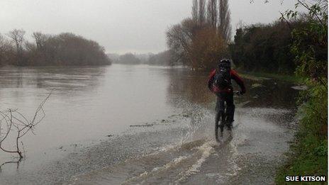 Cyclist riding through water on the River Thames tow path in Reading