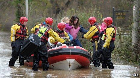 Crew Commander from Tewkesbury fire station Dave Webb (right) carries a 19-month-old child with her mother and three-year-old sister after they were rescued from their house in Gloucester