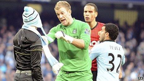 Manchester City's Joe Hart stops a fan who walked onto the pitch to confront Manchester United's Rio Ferdinand