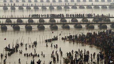 Hindu devotees take a dip at Sangam, the confluence of the Rivers Ganges, Yamuna and mythical Saraswati as others cross a make shift bridge, on one of the most auspicious day Makar Sankranti, the first day of the Maha Kumbh Mela, in Allahabad, India, Monday, Jan. 14, 2013.