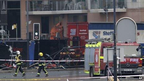 Firefighters walk past a section of a damaged crane