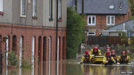 Firefighters pull a boat as they wade down a flooded street in St Asaph