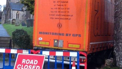 Lorry wedged between churchyard and house in Brompton Regis