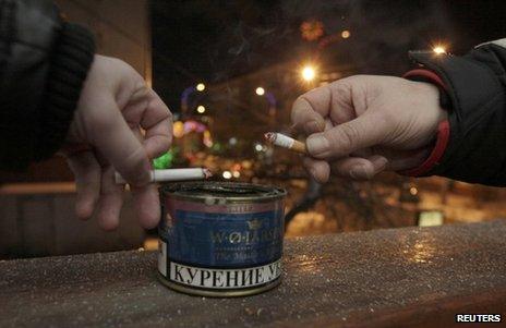 Men drop ash in a tin while smoking on the balcony of an office building in Krasnoyarsk, Russia, 24 January