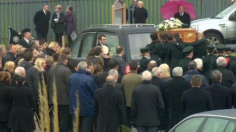 Pall bearers carry coffin behind hearse